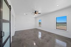 an empty room with two windows and a ceiling fan in the middle of the room