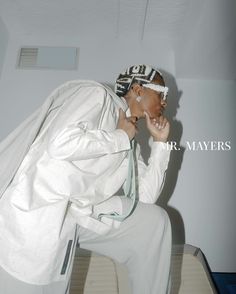 a man sitting on top of a wooden bench wearing a white suit and head scarf