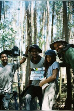 a group of people standing around each other in the woods with a camera and tripod