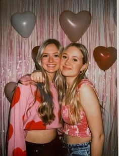 two young women standing next to each other in front of heart shaped balloon backdrops