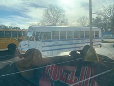 a white bus parked in a parking lot next to another bus on the side of the road