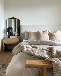 a bed with white linens and pillows in a bedroom next to a wooden table