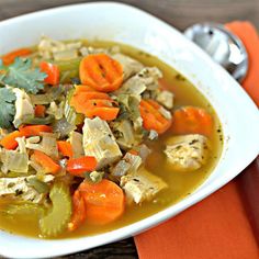 a white bowl filled with chicken, carrots and celery soup on top of an orange napkin