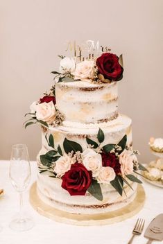 a three tiered cake with red and white flowers on the top is surrounded by silverware