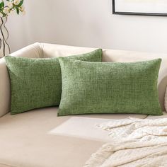 two green pillows sitting on top of a white couch next to a vase with flowers