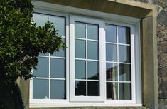 an open window on the side of a stone building next to a tree and shrub