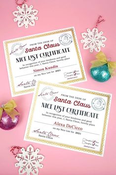 two christmas certificates sitting on top of a pink surface