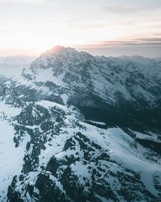 an aerial view of snow covered mountains at sunset