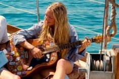 a woman sitting on top of a boat while playing a guitar