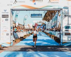 a woman is running in front of a crowd at the finish line with her arms up