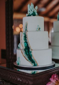 a three tiered white cake with green decorations on the top and bottom, sitting on a table in front of a mirror