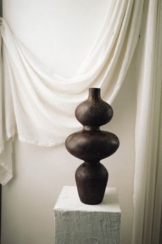 a tall brown vase sitting on top of a white block in front of a curtain