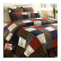 a bed with a plaid quilt on it and pillows in front of the bed cover