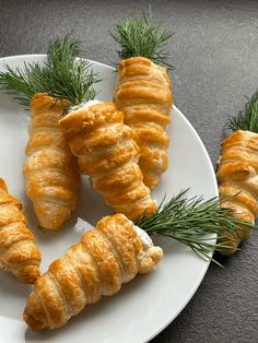 four croissants on a white plate with green sprigs and pine needles