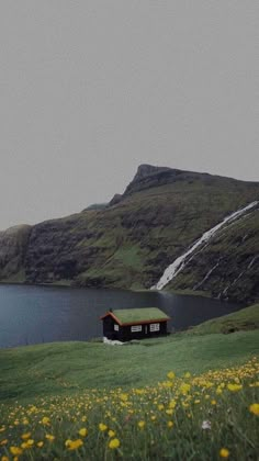 a small house sitting on top of a lush green hillside next to a lake and mountains