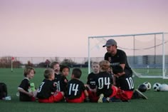 a man standing over a group of children on top of a soccer field next to a goal