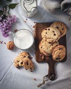 chocolate chip cookies on a cutting board next to a glass of milk and some nuts