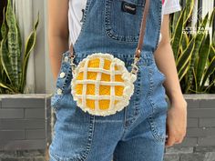 a person wearing overalls and holding a purse with a crochet design on it