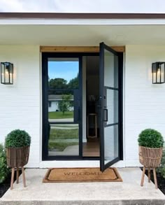 the front door to a white house with two planters on either side of it