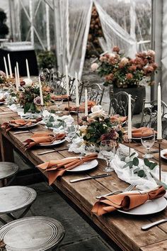 a long table set with plates and place settings for an outdoor dinner party in a greenhouse