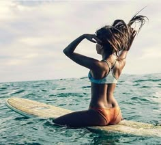 a woman sitting on a surfboard in the ocean with her hair blowing in the wind