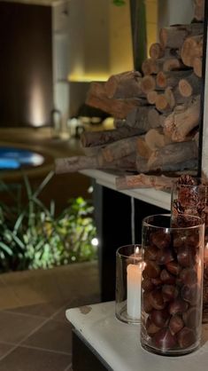 two candles are sitting on a table next to some logs and glass jars with nuts in them