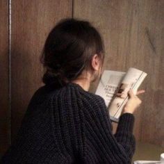 a woman is reading a book while sitting on a toilet seat in front of a wooden paneled wall