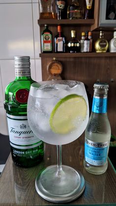 a glass filled with ice and lime sitting on top of a table next to bottles