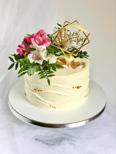 a white cake with pink flowers and gold lettering on top is sitting on a plate