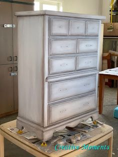 a white dresser sitting on top of a wooden table next to a metal refrigerator freezer