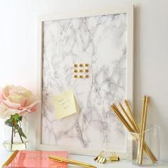 there is a marble board with gold pens on it next to a vase and flowers