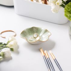 a white table topped with flowers and two wedding rings on top of a green bowl