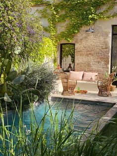 an outdoor living area next to a swimming pool with wicker furniture and greenery