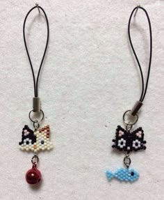 two small beaded earrings with cats and fish charms hanging from black cord on white background