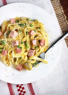 a white plate topped with pasta and ham on top of a checkered table cloth