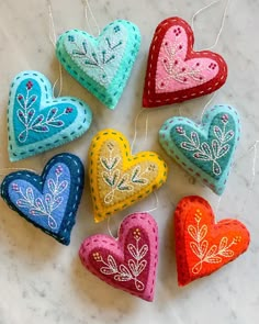 six heart shaped ornaments hanging from strings on a marble counter top with beads and thread