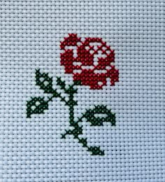 a cross stitch rose with green leaves and red beads on the bottom is shown in white