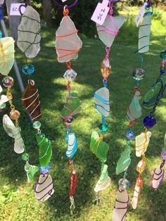 a group of colorful glass wind chimes hanging from a line in the grass with price tags on them