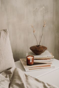 a stack of books sitting on top of a bed next to a candle