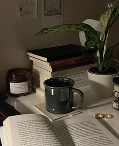 an open book sitting on top of a table next to a cup and potted plant