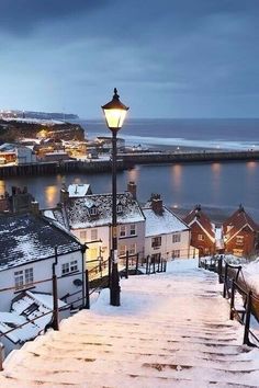 snow covered steps leading up to the water and buildings in front of them with lights on