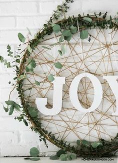 a christmas wreath with the word joy written on it and greenery in front of a white brick wall