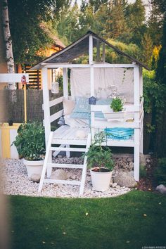 a white gazebo sitting in the middle of a lush green yard with potted plants