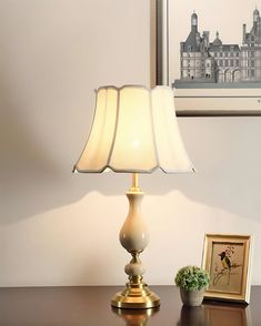 a lamp sitting on top of a wooden table next to a framed picture and potted plant