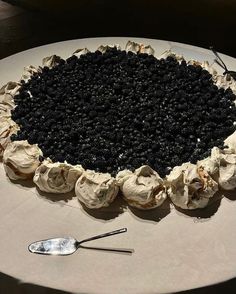 a cake with blackberries and cream frosting sitting on a table next to a spoon