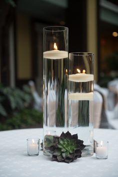 three candles are placed in glass vases with succulents on the table