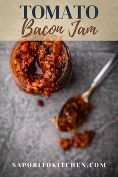 a jar filled with bacon jam on top of a gray surface next to a spoon