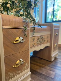 an antique dresser with gold handles and flowers on it's top, in front of a window