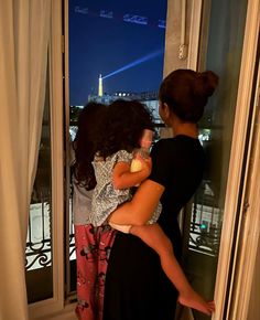 two girls are looking out the window at the city lights in the distance, and one girl is holding onto her mother's shoulders