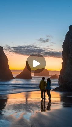 two people standing on the beach at sunset looking out to sea stacks in the distance